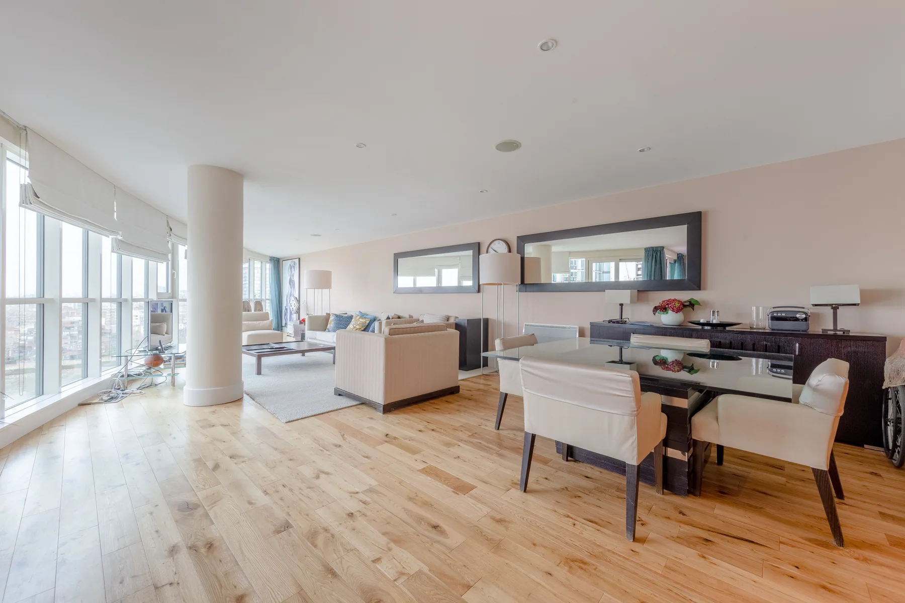 Una sala-comedor de planta abierta con grandes ventanas y suelo de madera clara.
