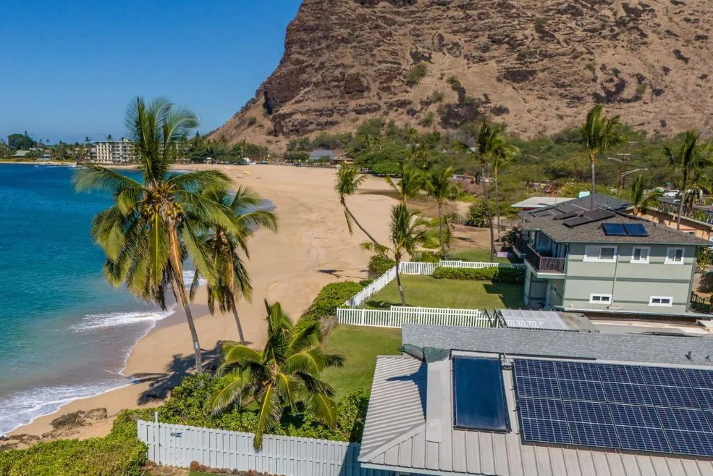 Vista aérea de una propiedad frente a la playa, junto a una costa arenosa y una ladera rocosa.