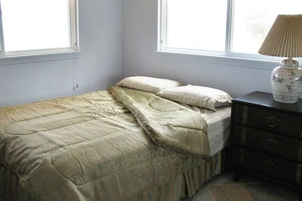 Un dormitorio con una cama vestida con ropa de cama clara junto a una cómoda oscura.