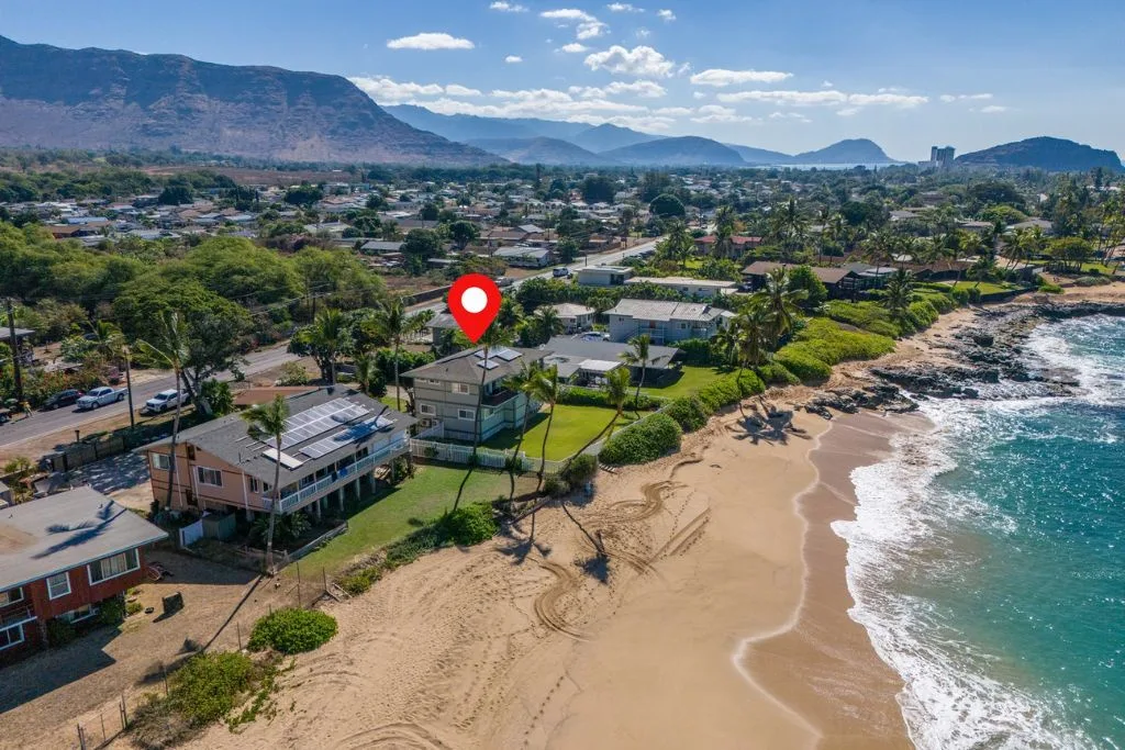 Vista aérea de un barrio costero junto a una playa de arena y montañas.