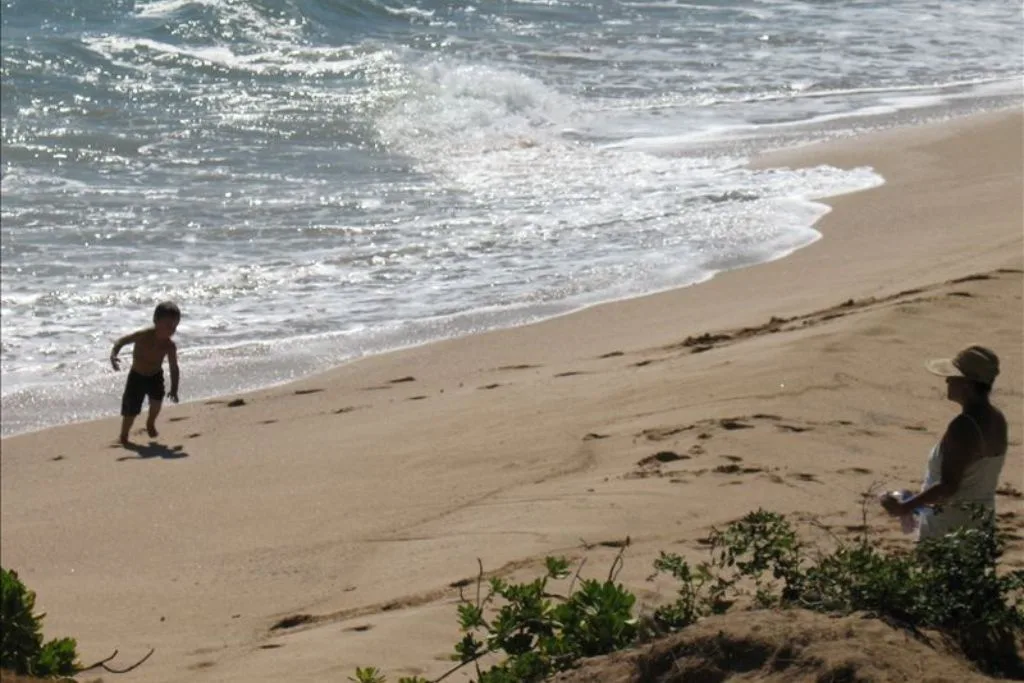 Una playa de arena con olas llegando a la orilla y personas cerca del agua.