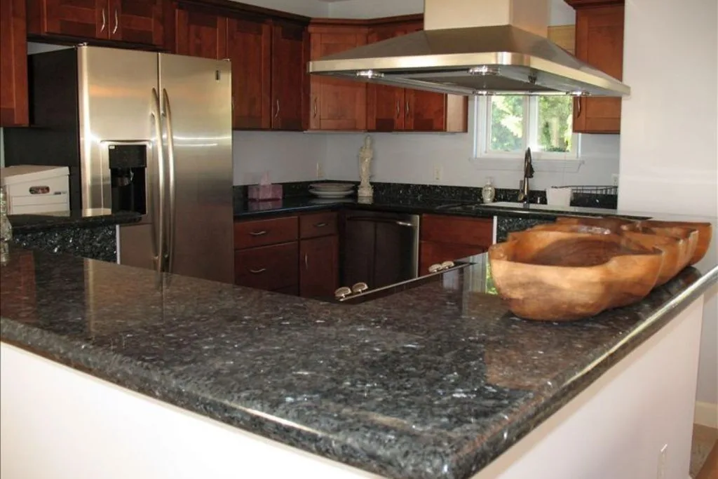 Una cocina con encimeras oscuras, armarios de madera y un refrigerador de acero inoxidable.