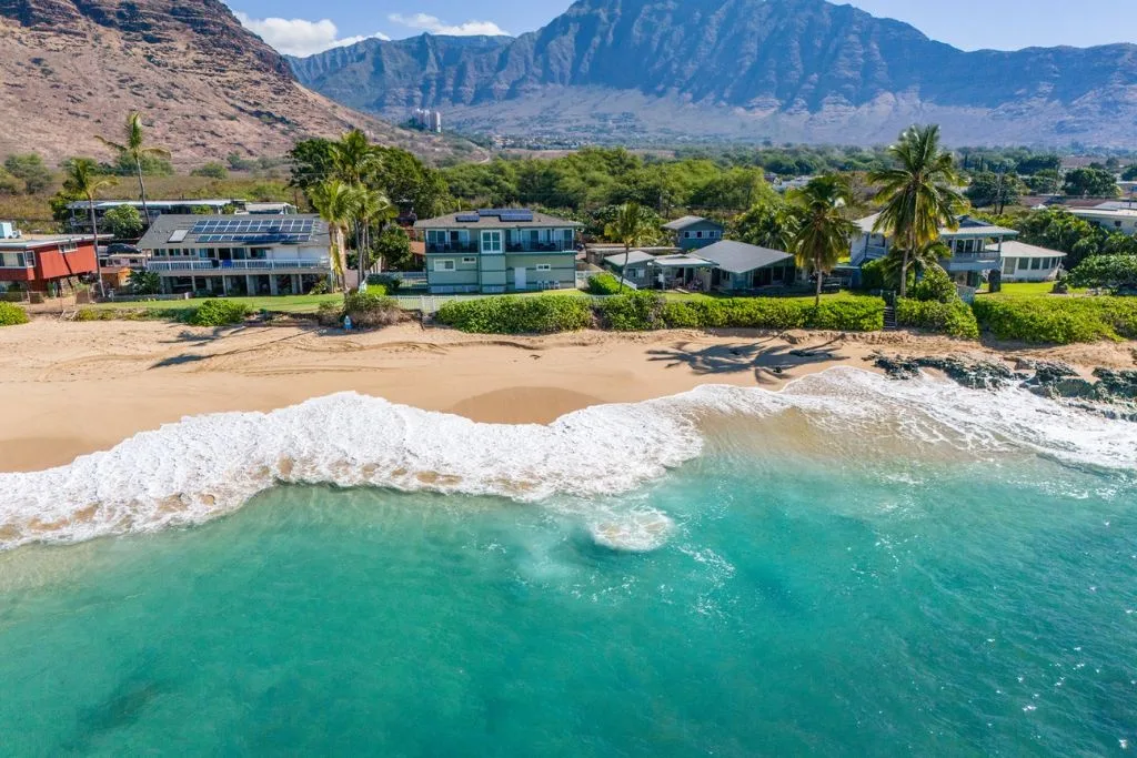 Vista aérea de una playa de arena con olas turquesas y casas junto a la costa.