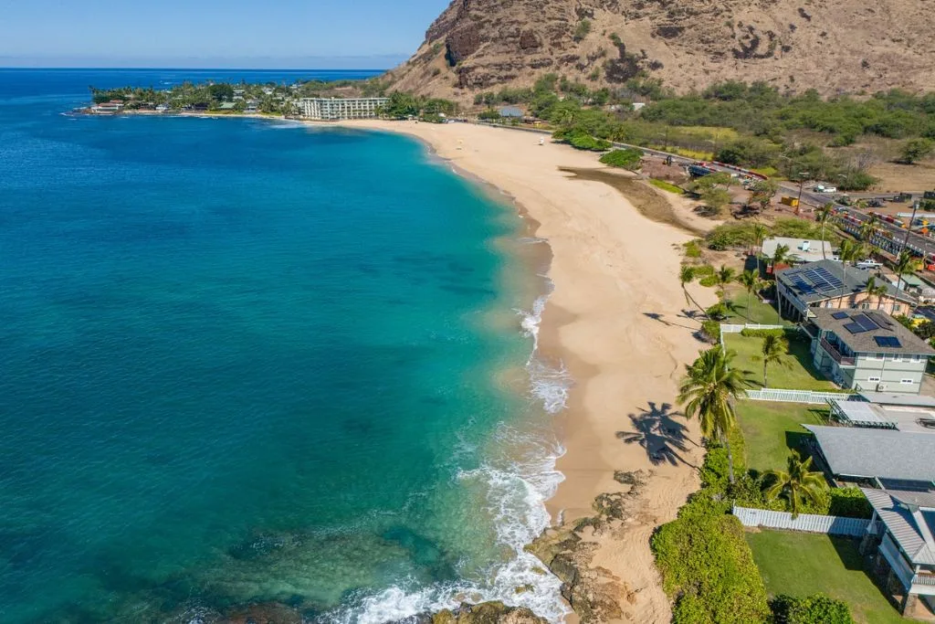 Vista aérea de una playa de arena junto a aguas turquesas y edificios costeros.