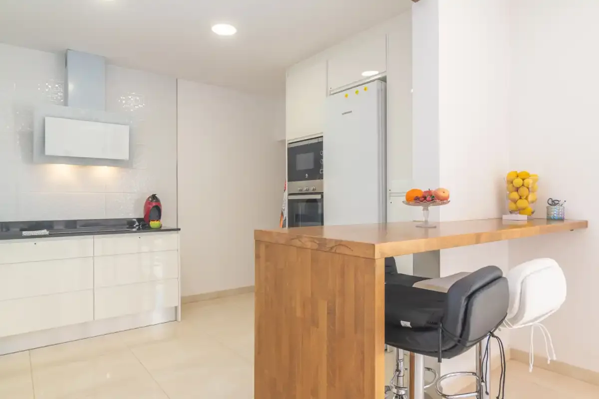 A bright kitchen with white cabinets and a wooden island with bar seating.