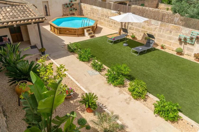 A landscaped outdoor patio has a small pool, lawn, loungers, and a sun umbrella.