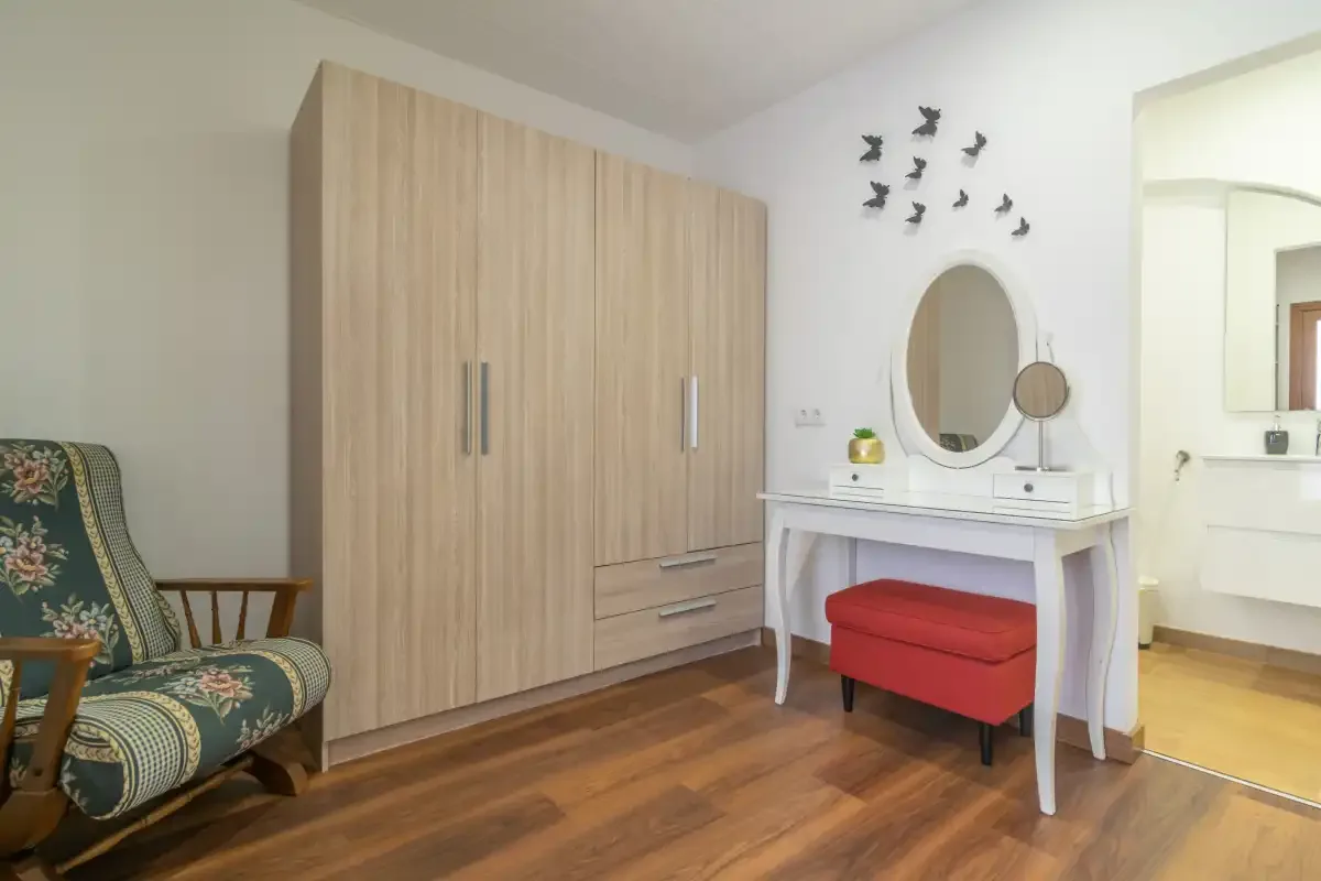 A bedroom with a wooden wardrobe, vanity table, and upholstered seating.