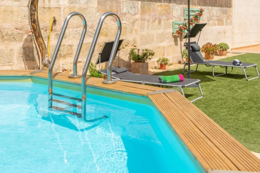 A swimming pool beside lounge seating and a wooden deck.