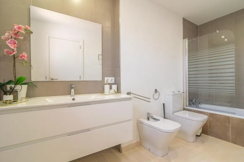 A bright bathroom with a long vanity, two sinks, and a glass shower.