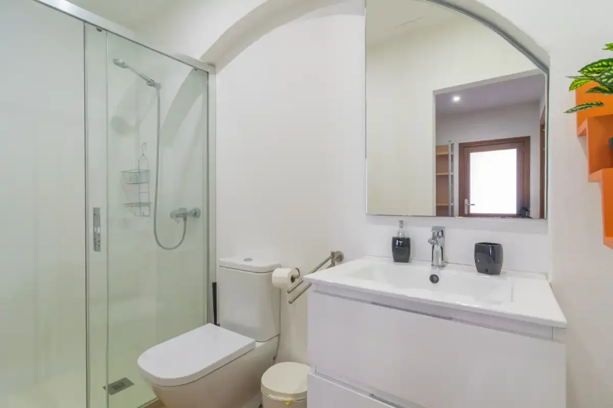 A bathroom with a shower, toilet, and sink beneath a large mirror.