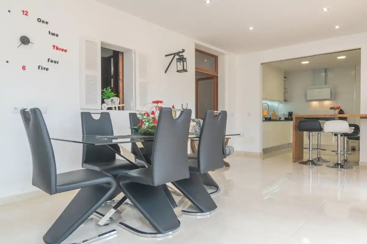 A bright dining area with dark seating and an open kitchen beyond.