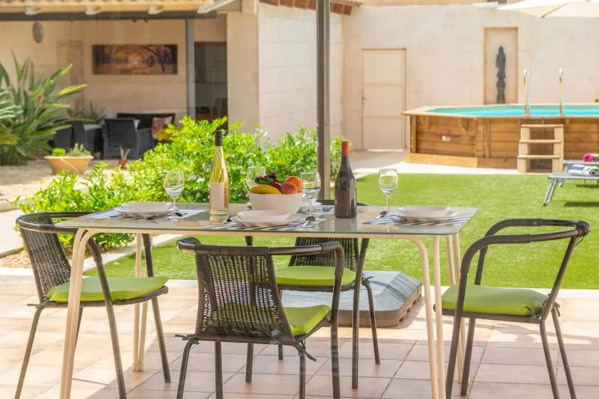 A patio dining area with a table set beside a garden and swimming pool.