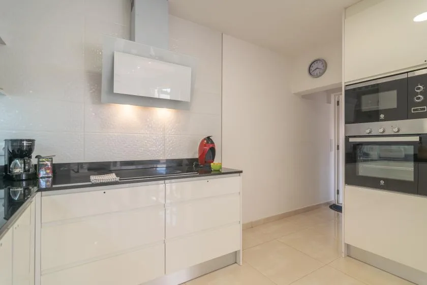 A bright modern kitchen with white cabinets, a dark countertop, and built-in appliances.