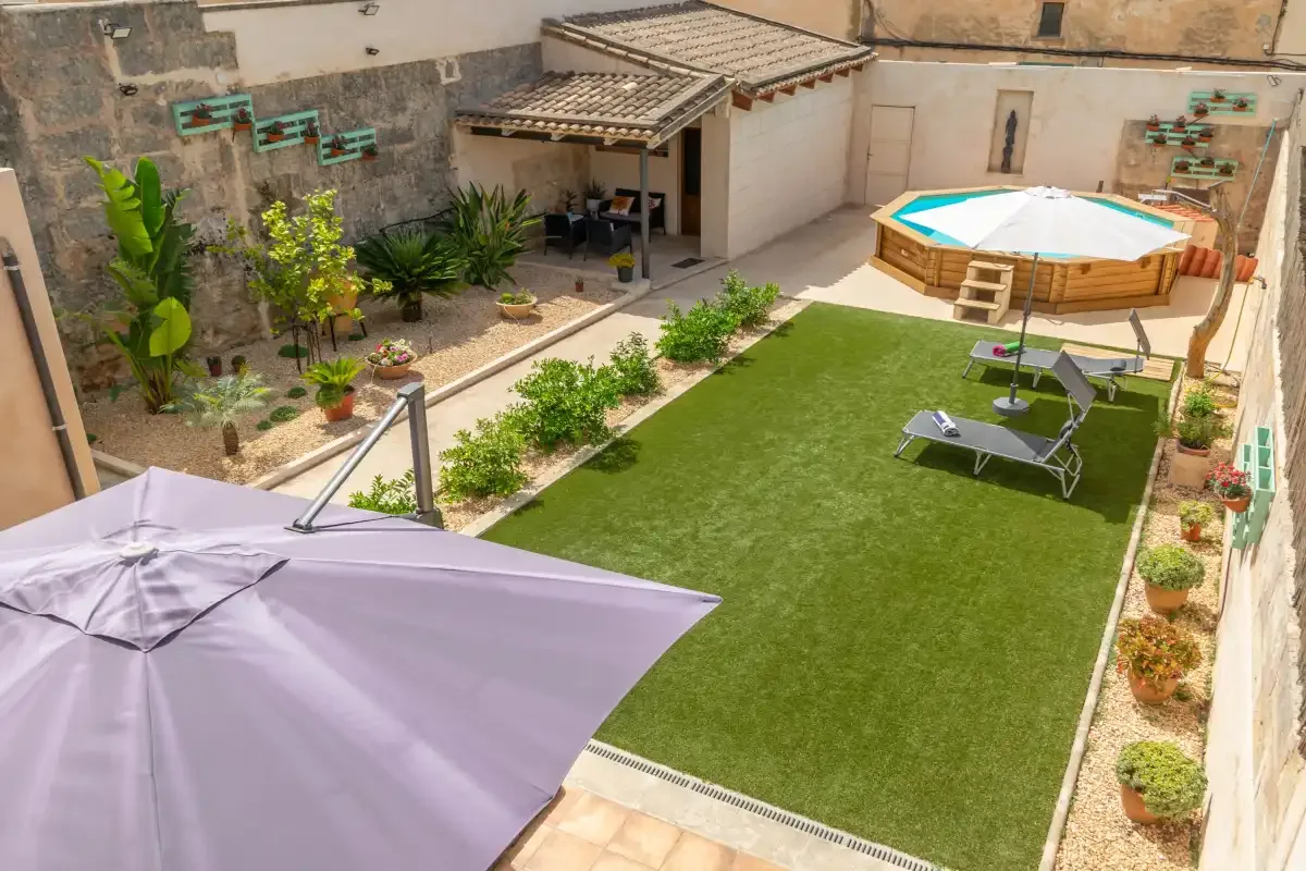 A courtyard garden with a rectangular lawn, patio seating, and a raised hot tub.