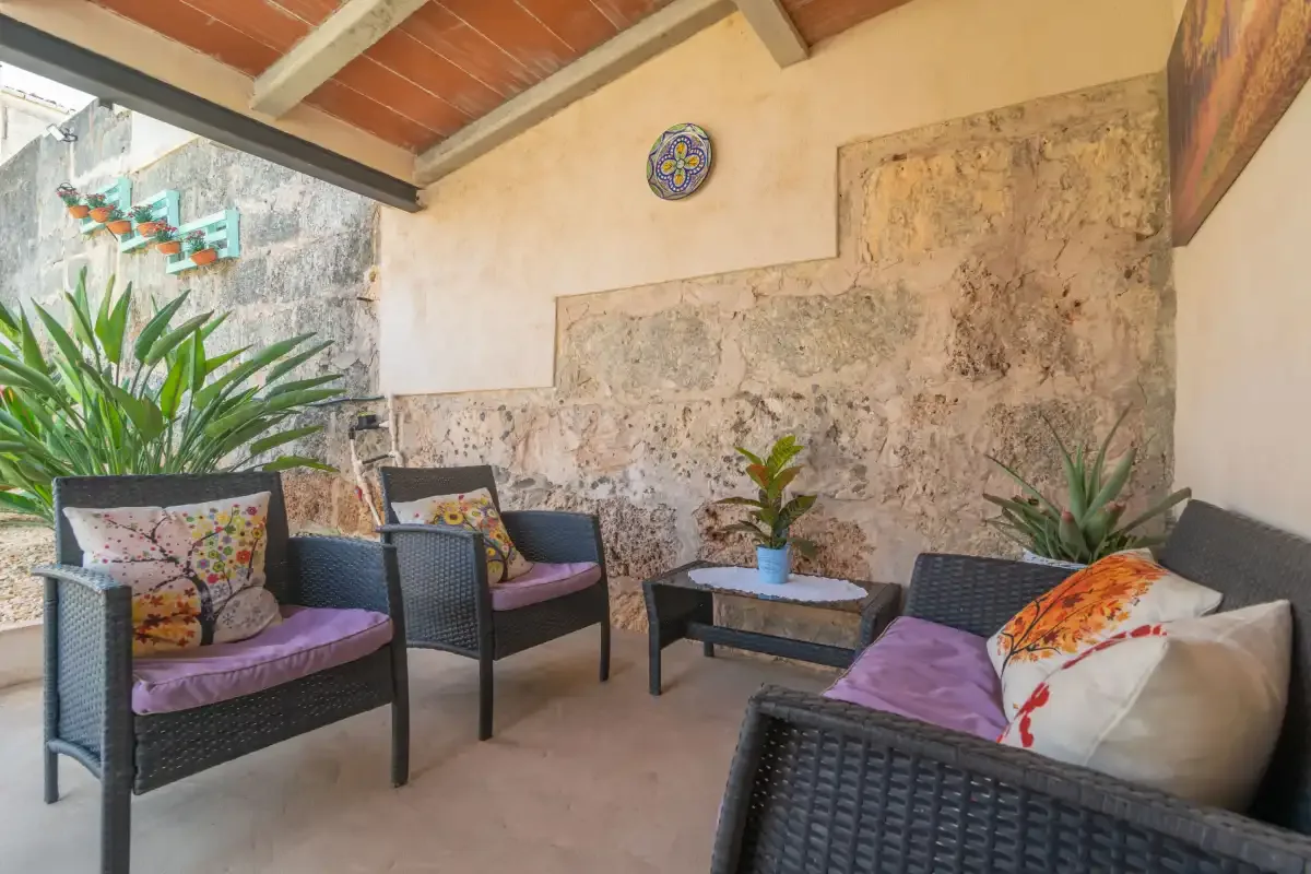 A covered patio seating area with dark woven furniture and potted plants.
