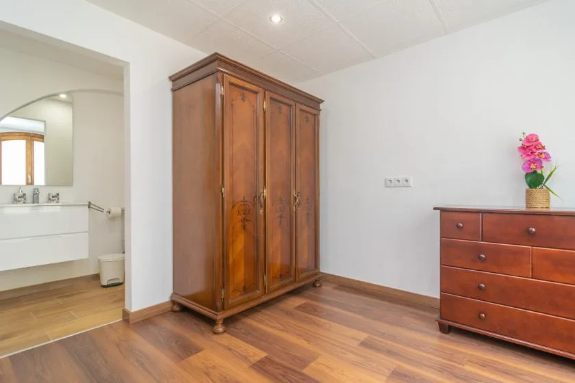 A bedroom with a wooden wardrobe and chest of drawers.
