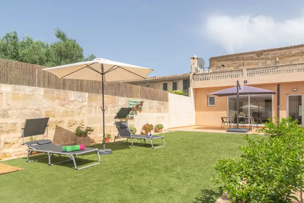 A sunny outdoor patio with lounge seating, umbrellas, and a lawn beside the house.