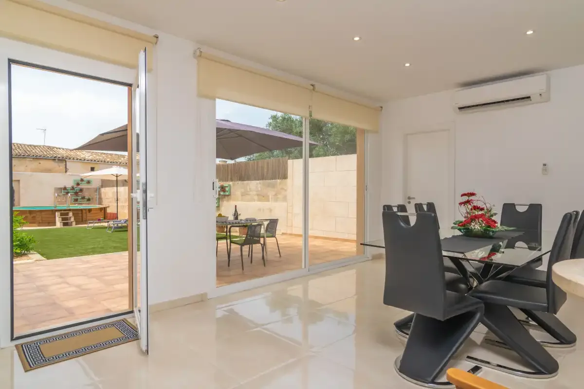 A bright dining area opens onto a tiled patio and garden through wide glass doors.