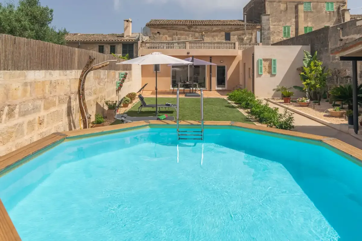 An outdoor swimming pool sits beside a patio and tan stone buildings.