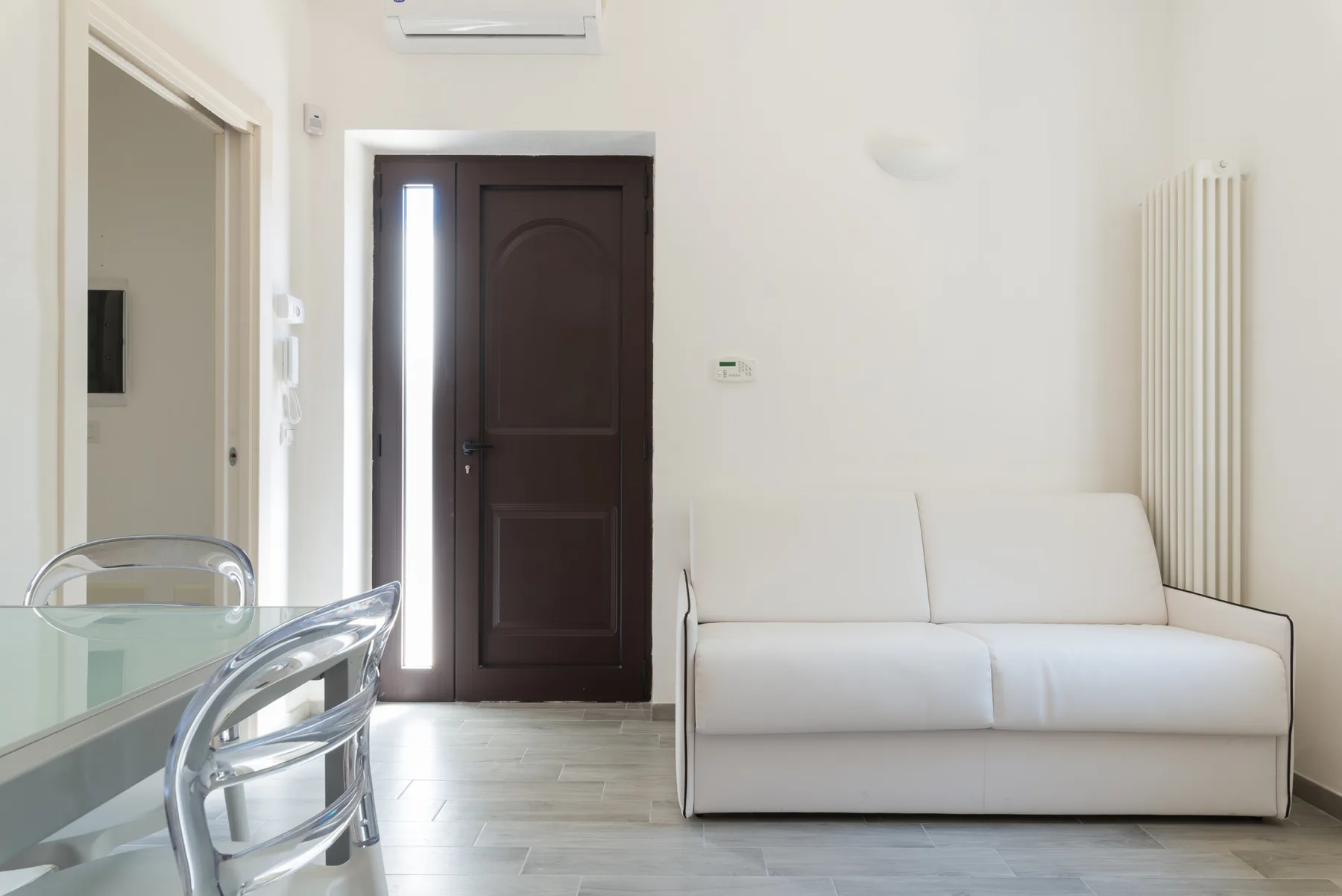 Una sala luminosa con un sofá blanco y una mesa de comedor de vidrio.
