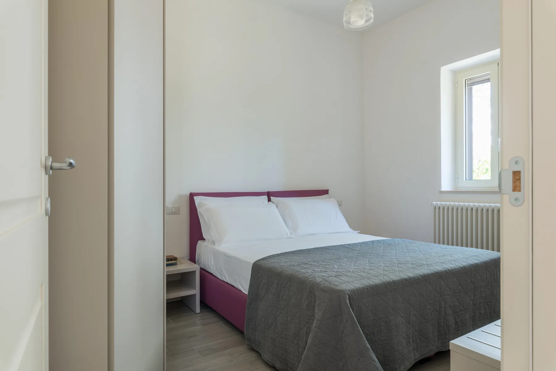 Un dormitorio con una cama doble, almohadas blancas y una colcha gris.