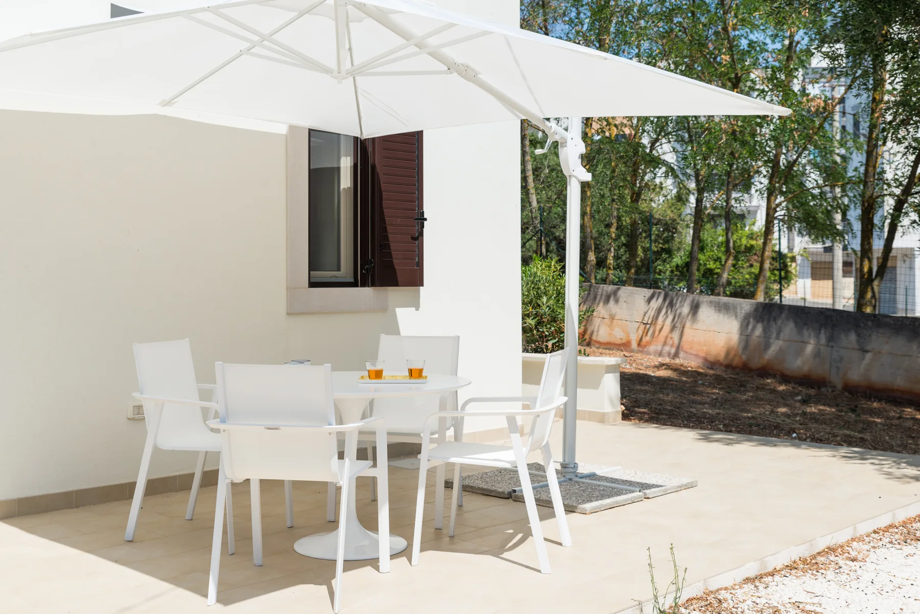 Una zona de comedor al aire libre está bajo una gran sombrilla blanca junto a un edificio blanco.
