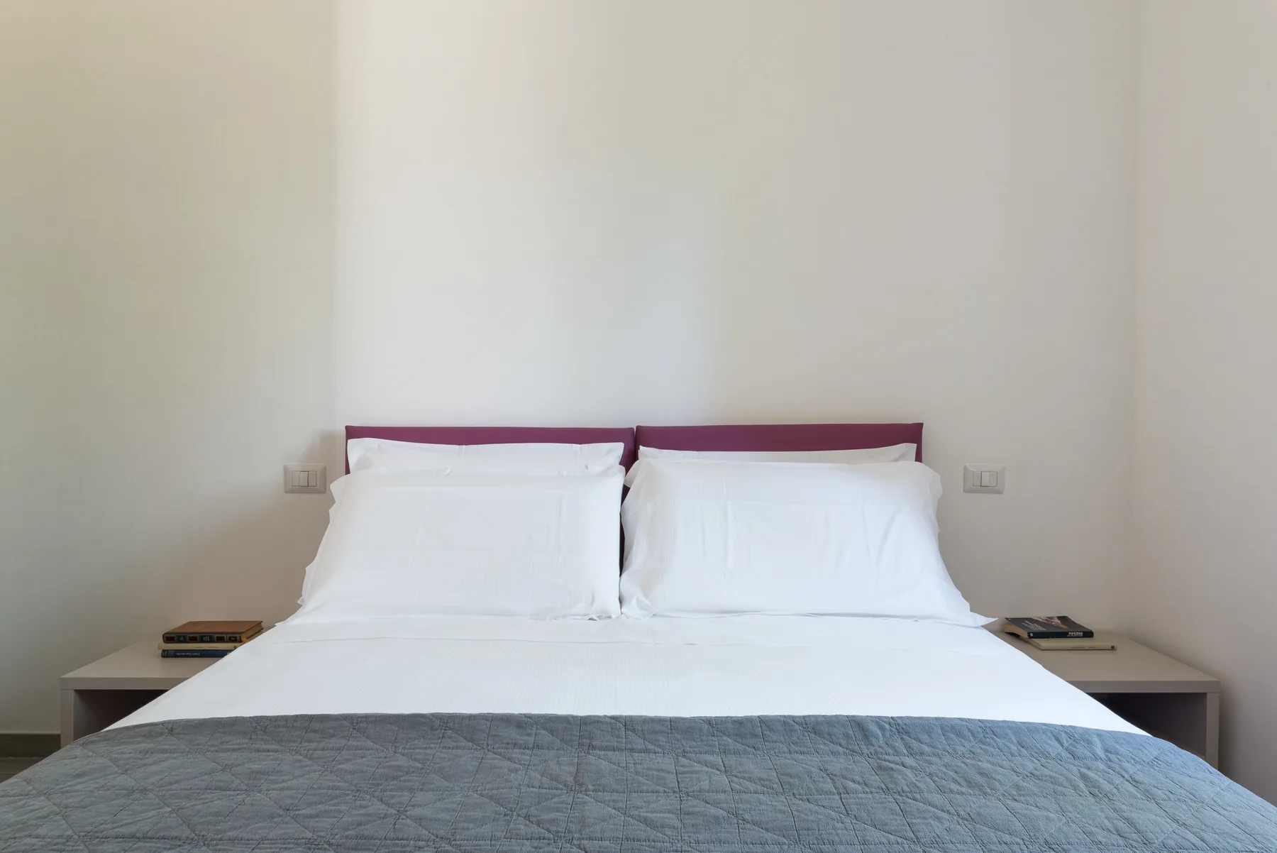 Dormitorio con una cama vestida con ropa de cama blanca y una colcha gris.