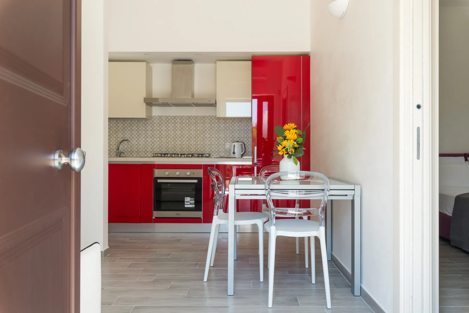 Comedor con mesa de vidrio y sillas junto a una cocina roja.