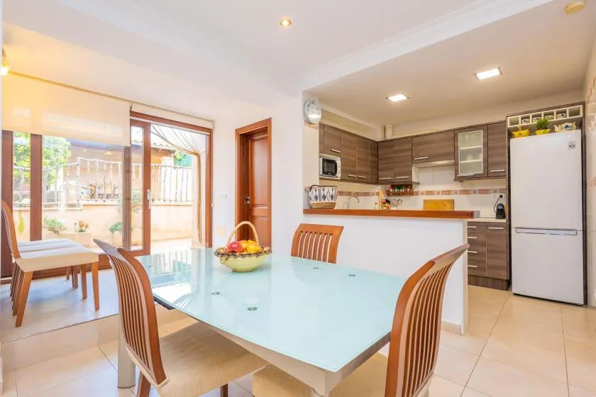Un comedor se abre a una cocina, con una mesa de vidrio en primer plano.