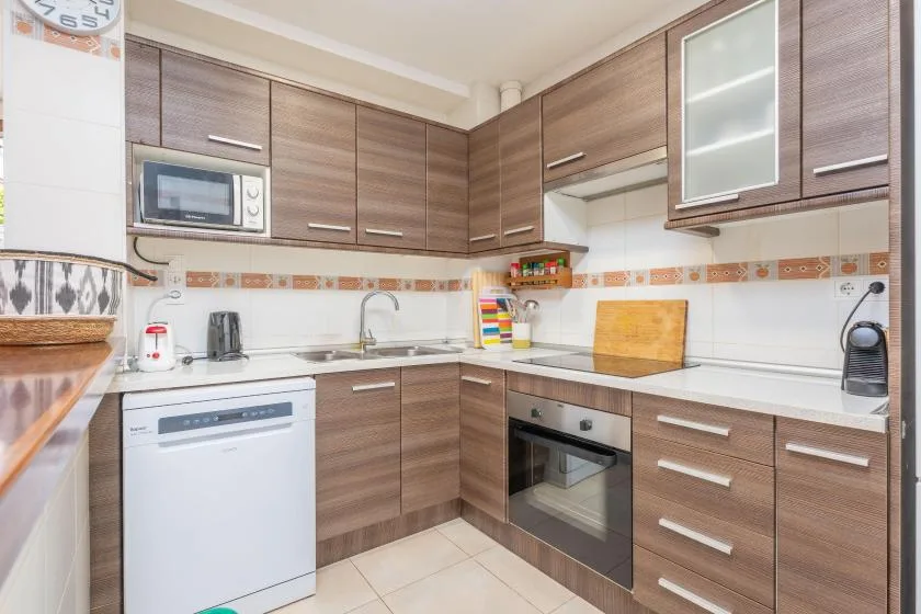 Una cocina con muebles en tonos de madera, un microondas y electrodomésticos integrados.