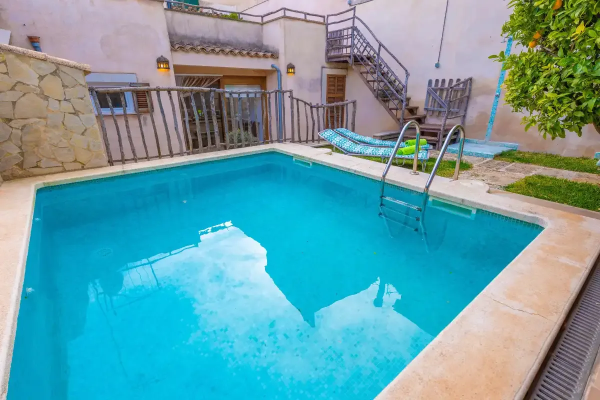 Una piscina al aire libre con una escalera metálica y asientos en el patio.