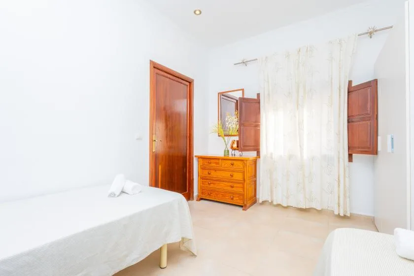 Un dormitorio luminoso con camas, muebles de madera y cortinas translúcidas.