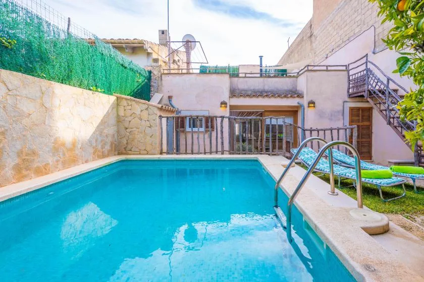 Una piscina al aire libre junto a un patio, con escalones y asientos cerca.