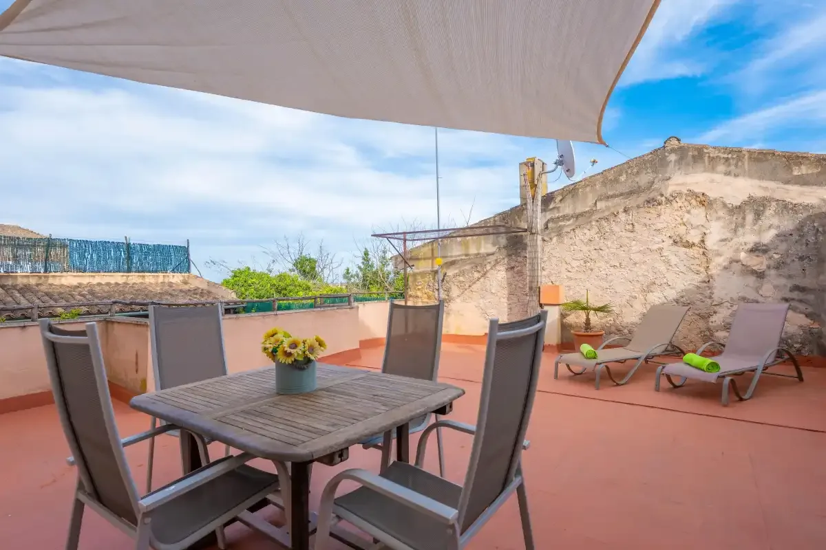 Una terraza en la azotea con mesa de comedor a la sombra y asientos de descanso.