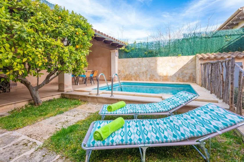 An outdoor pool beside patterned loungers, a leafy tree, and a small patio.