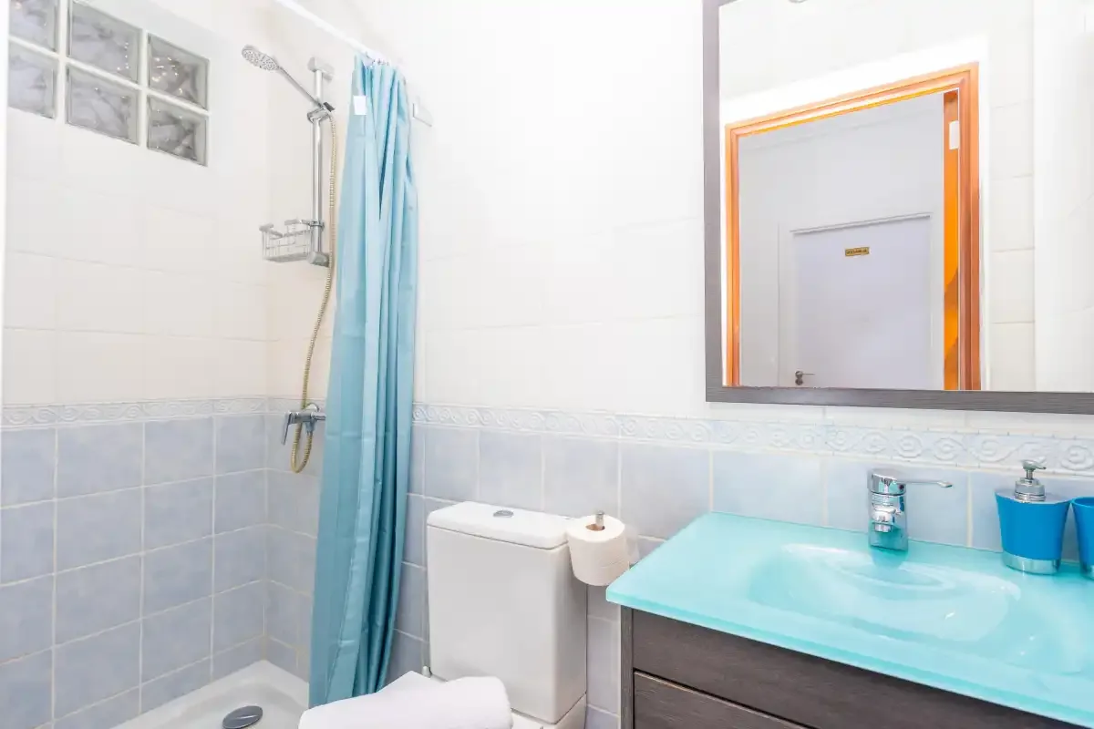 Un baño con ducha, inodoro y lavabo turquesa.