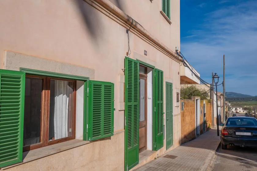 Una calle con un edificio claro y contraventanas verdes junto a la acera.