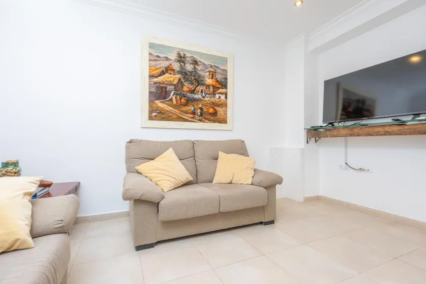 Una sala luminosa con asientos beige y un televisor montado en la pared.