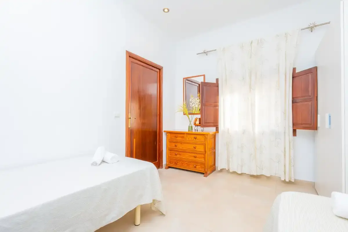 Un dormitorio luminoso con una cama, una cómoda de madera y una ventana con cortinas.