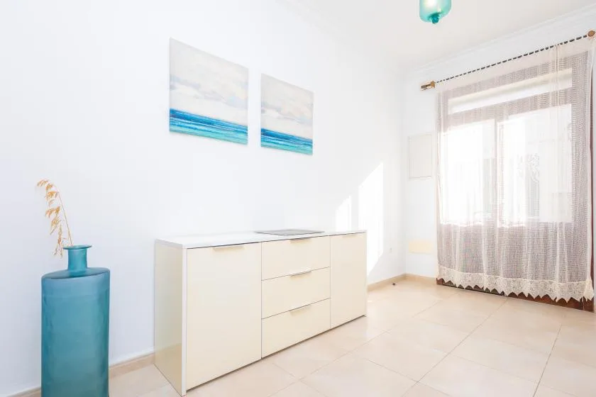 Una habitación luminosa con un mueble bajo, cuadros y una ventana con cortinas.