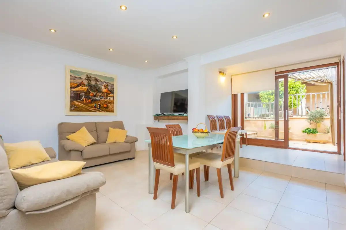 Una luminosa sala de estar y comedor con asientos, una mesa y puertas de vidrio hacia un patio.