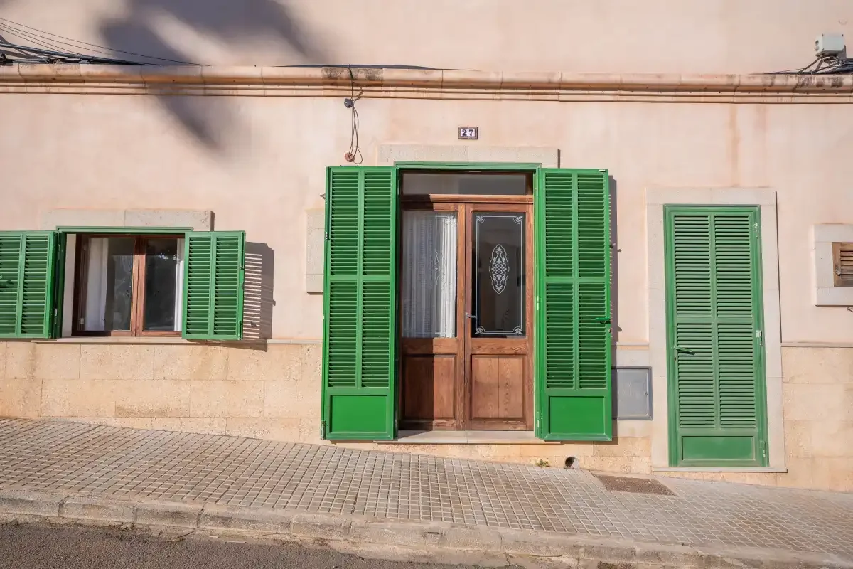 La fachada de un edificio color melocotón tiene contraventanas verdes y una puerta de entrada de madera.
