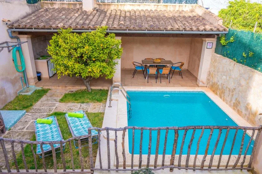 Una piscina en el patio junto a una terraza cubierta con mesa y asientos.