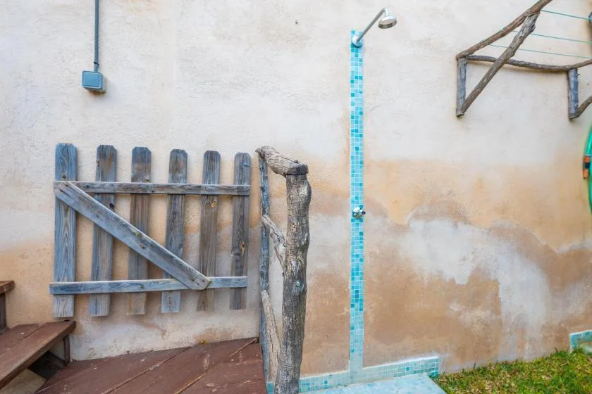 Zona de ducha exterior con una columna de azulejos junto a una cerca de madera.