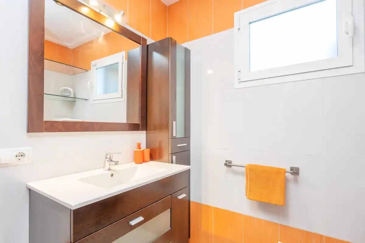 Un baño con lavabo, espejo y detalles de azulejos naranjas.