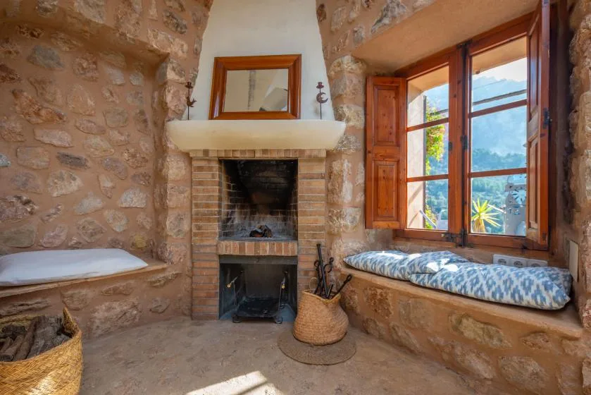 A rustic stone room with a fireplace and a cushioned window seat.