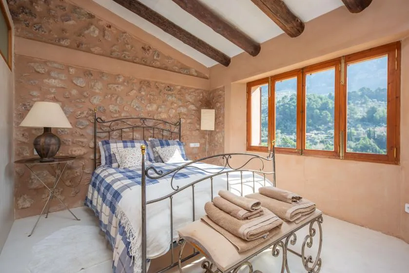 A bedroom with a metal bed, folded towels, and a large window overlooking green hills.