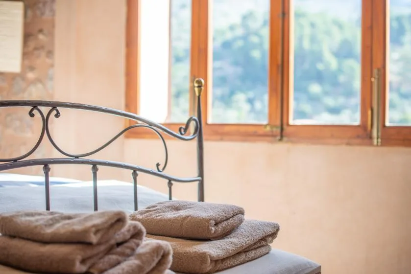 A bedroom with a metal bed frame and folded towels beside a window.