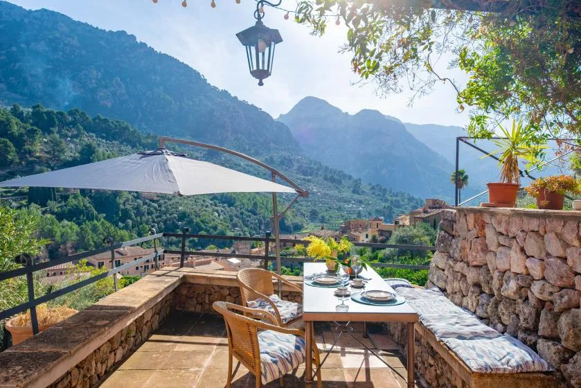 A mountain-view terrace has a dining table, seating, and a sunshade.