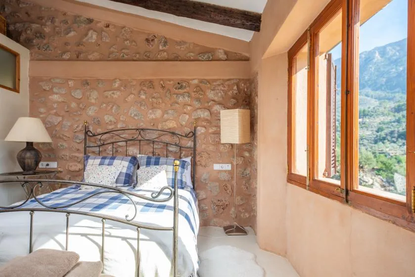 A bedroom with a metal bed, stone walls, and large windows overlooking a mountain landscape.